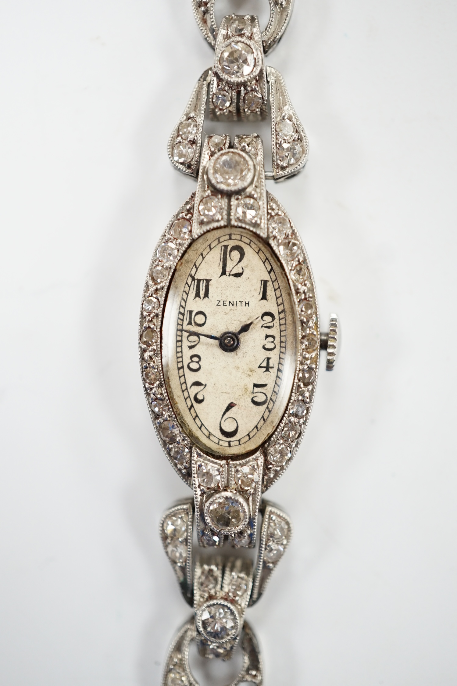 A lady's Zenith white metal and diamond cluster set manual wind oval cocktail watch, on a twin fabric strap, 15cm, gross weight 16.7 grams. Fair condition.